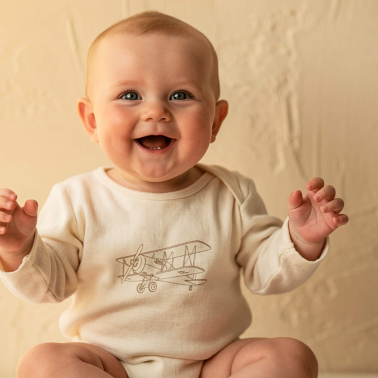 Baby wearing a onesie with an airplane design on a beige background