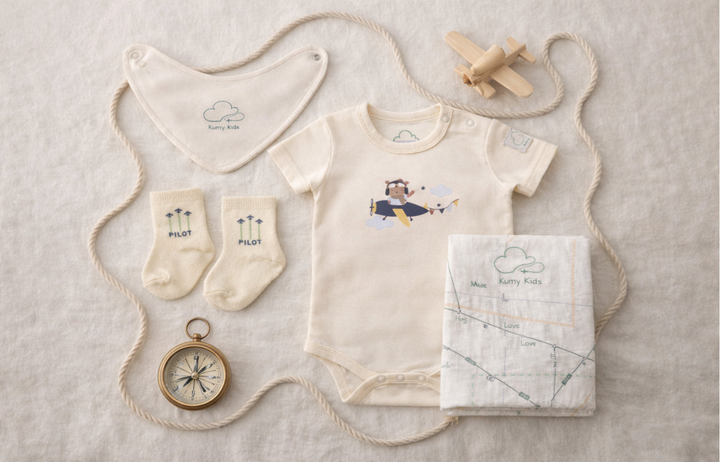 Baby clothing and accessories including a onesie, socks, bib, and blanket on a textured surface.