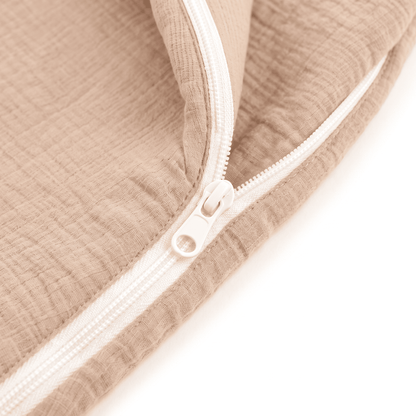 Close-up of a beige muslin fabric item with a white zipper, showing the textured fabric and zipper details against a white background.